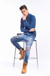 Male Model In Denim Jeans Sitting On A Chair . Studio Shoot Stock Photo