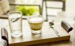 Cappuccino Coffee Cup With Glass Of Water Serving On Wooden Tray On Coffee Table Stock Photo