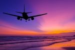 Silhouetted Commercial Airplane Flying Above The Sea At Sunset Stock Photo