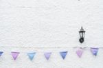 Colorful Party Flags Bunting Hanging On White Wall Background With Wall Lamp Light. Minimal Hipster Style Design Stock Photo