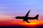 Silhouetted Commercial Airplane Flying At Sunset Stock Photo