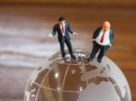 Miniature Businessman Stand On Globe Of Glass With Wooden Backgr Stock Photo