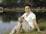 Woman Sitting On Green Field By Lake Stock Photo