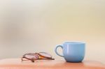 Blue Cup And Eyeglass On The Table Stock Photo