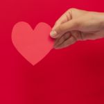 Pink Paper Heart In Hand On The Red Background Stock Photo