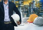 Engineering Man Standing With White Safety Helmet Against  Oil R Stock Photo