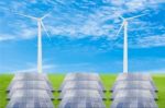 Solar Panels And Wind Turbine On Green Grass Field Against Blue Stock Photo