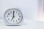 White Square Clock On White Bed Stand With White Wallpaper Background, Morning Time In Minimal Style Decoration Stock Photo