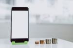 Smartphone Blank Screen Placed On A Vertical Green Stand, And The Coins Are Arranged In A Row. Represents The Growth Of Financial Stock Photo