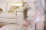 Young Girl Sitting In A Sofa And Using Phone Behind The Glass Window Stock Photo