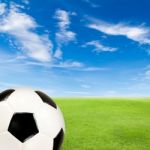 Soccer Ball With Green Grass Field Against Blue Sky Stock Photo