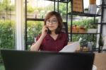 A Young Lady Wears Glasses Working On Laptop And Talking On A Mo Stock Photo