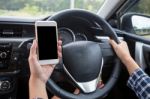 Young Female Driver Using Touch Screen Smartphone And Hand Holding Steering Wheel In A Car Stock Photo