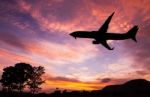 Silhouetted Commercial Airplane Flying At Sunset Stock Photo