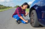 Young Woman Changing Car Wheel On Country Road Stock Photo