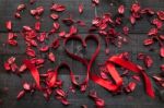 Red Bow Surrounded By Dried Petals On Wooden Background Stock Photo