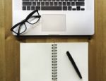 Modern Laptop With Paper Note Book With Pen And Glasses On Wood Stock Photo