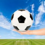 Hand Holding Soccer Ball With Soccer Field And Blue Sky Stock Photo