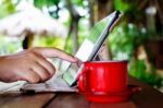 Finger Touching On Tablet With Red Cup On Table In Garden Stock Photo