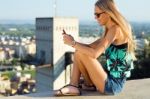 Beautiful Blonde Girl Sitting On The Roof With Mobile Phone Stock Photo