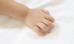 Back Hand Of Asian Baby On White Bedcovers Stock Photo