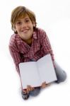 Front View Of Boy Sitting On Books And Reading Book Stock Photo