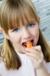 Cute Little Girl Eats Carrot And Looking At The Camera Stock Photo