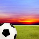 Soccer Ball With Green Grass Field Against Sunset Sky Stock Photo