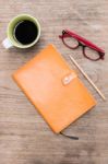 Blank Orange Leather Diary,glasses And A Cup Of Coffee On Wooden Desk Stock Photo