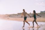 A Couple Is Running On Beach While The Sun Is Set Stock Photo