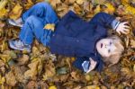 Toddler Blond Boy With Blue Eyes Lays On Bed Of Autumn Fallen Le Stock Photo