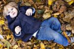 Toddler Blond Boy With Blue Eyes Lays On Bed Of Autumn Fallen Le Stock Photo