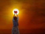 Women Gently Hold Red Heart To The Sun Stock Photo