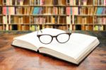 Open Book With Glasses On The Desk Against Library Stock Photo