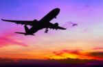 Silhouetted Commercial Airplane Flying At Sunset Stock Photo