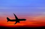 Silhouetted Commercial Airplane Flying At Sunset Stock Photo