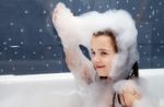 Little Girl Sitting In A Bath And Plays With Soap Suds Stock Photo