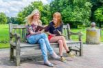 Dutch Girls Sitting On Wooden Bench In Park Reading Books Stock Photo