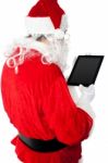 Back View Of Santa Looking At Tablet Device Screen Stock Photo