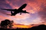 Silhouetted Commercial Airplane Flying At Sunset Stock Photo