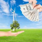 Hand Holding Wind Turbine With Tree And Us Dollars Banknote Stock Photo