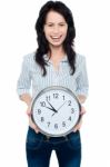 Cheerful Brunette In Casual Presenting A Wall Clock Stock Photo