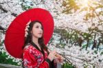 Asian Woman Wearing Traditional Japanese Kimono With Red Umbrella And Cherry Blossom Stock Photo