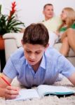 Young Boy Studying With Family In The Background Stock Photo