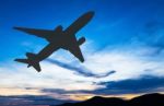 Silhouetted Commercial Airplane Flying At Sunset Stock Photo