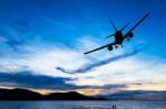 Silhouetted Commercial Airplane Flying Above The Sea At Sunset Stock Photo