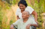 Senior Woman Pushing Her Disabled Husband On Wheelchair Stock Photo