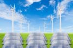 Solar Panels And Wind Turbine On Green Grass Field Against Blue Stock Photo