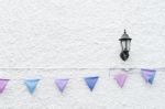 Colorful Party Flags Bunting Hanging On White Wall Background With Wall Lamp Light. Minimal Hipster Style Design Stock Photo