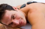 Smiling Young Man Receiving Hot Stone Treatment Stock Photo